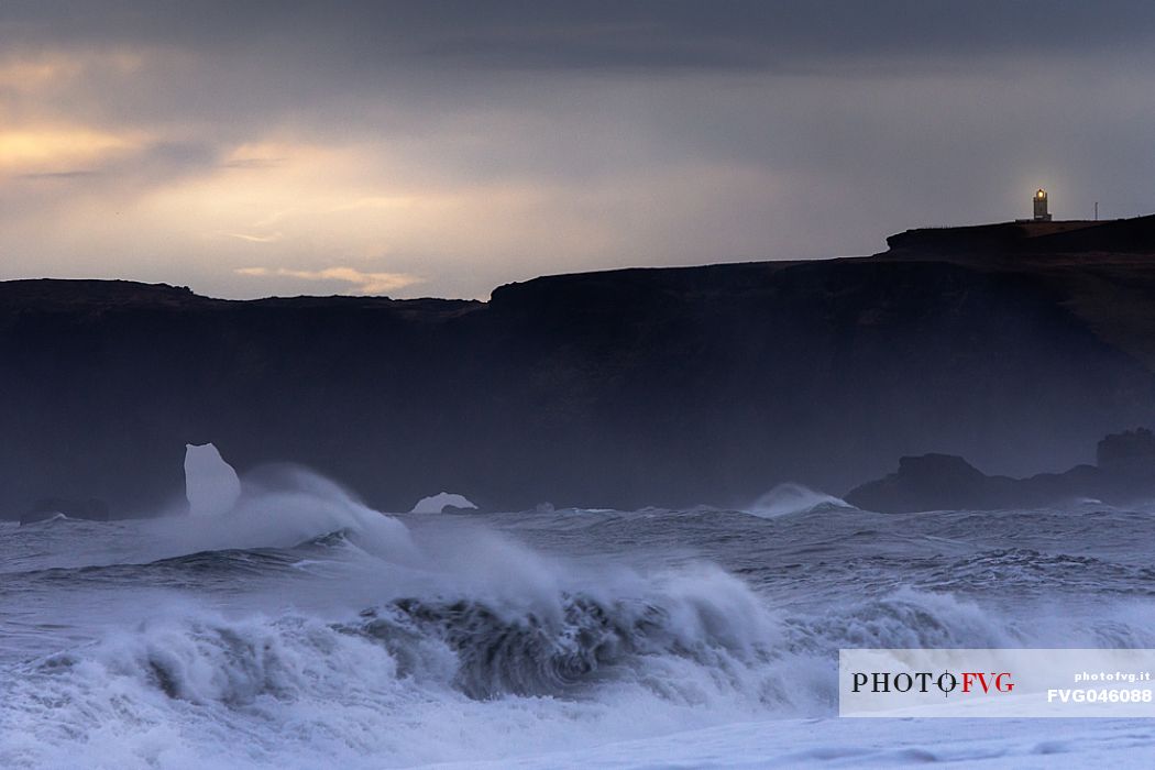 Stormy sea and lighting lighthouse at the Cape Dyrhlaey, Myrdalur, Iceland, Europe